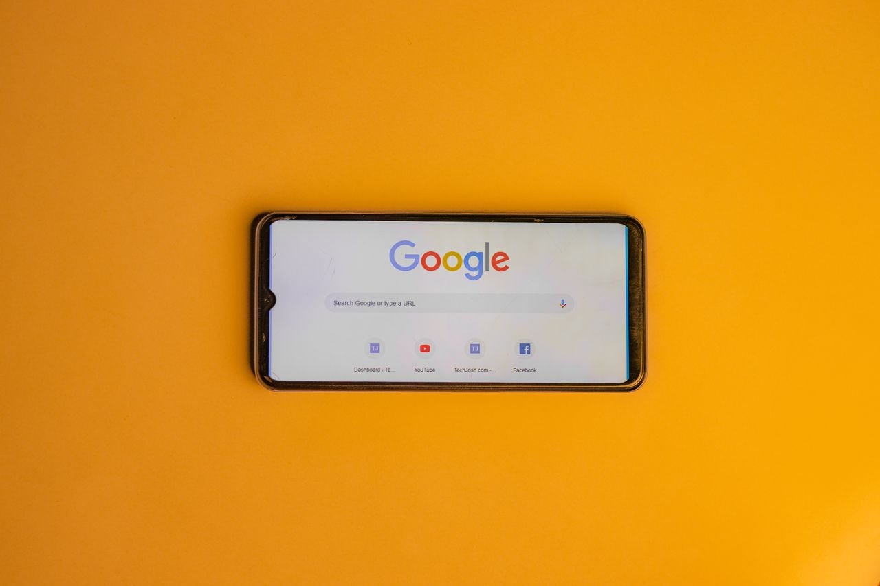 Smartphone displaying Google search page on a vibrant yellow background.
